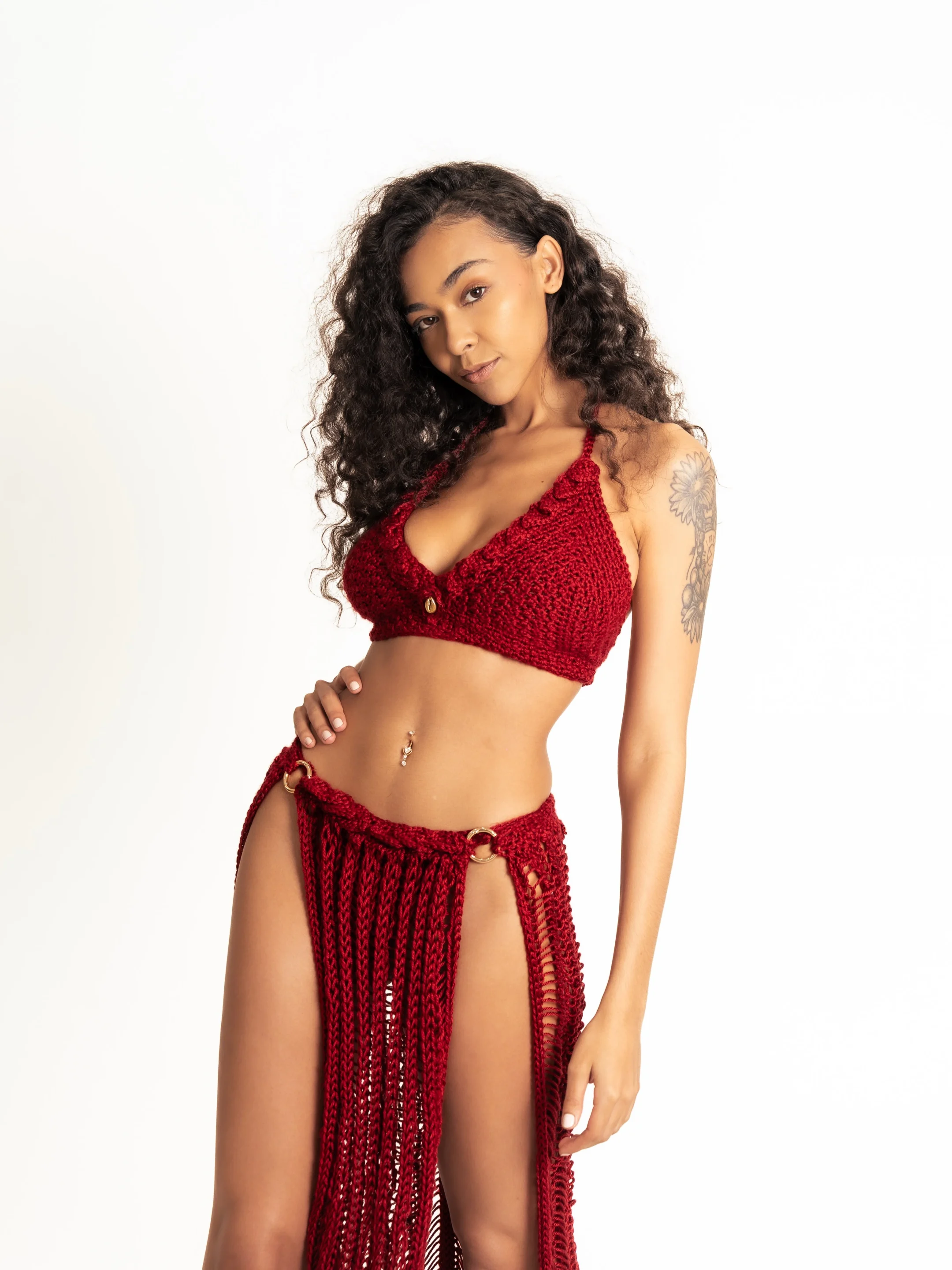 Woman with curly hair posing in a red crochet bralette and fringed skirt against a white backdrop at a Miami photo studi | Creative Canvas Photo Studio Miami Woman with curly hair posing in a red crochet bralette and fringed skirt against a white backdrop at a Miami photo studio