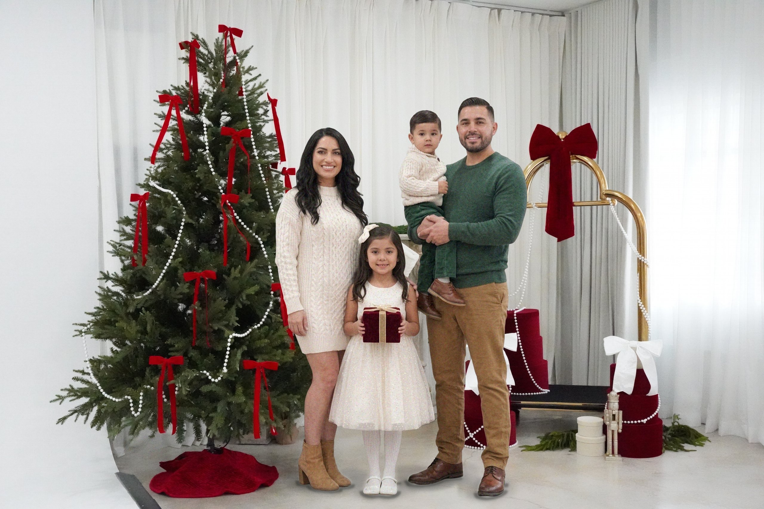 Christmas photography in Miami | Creative Canvas Photo Studio Miami Set de fotos navideñas en Miami familia de cuatro entre un árbol con lazos rojos y un carrito dorado