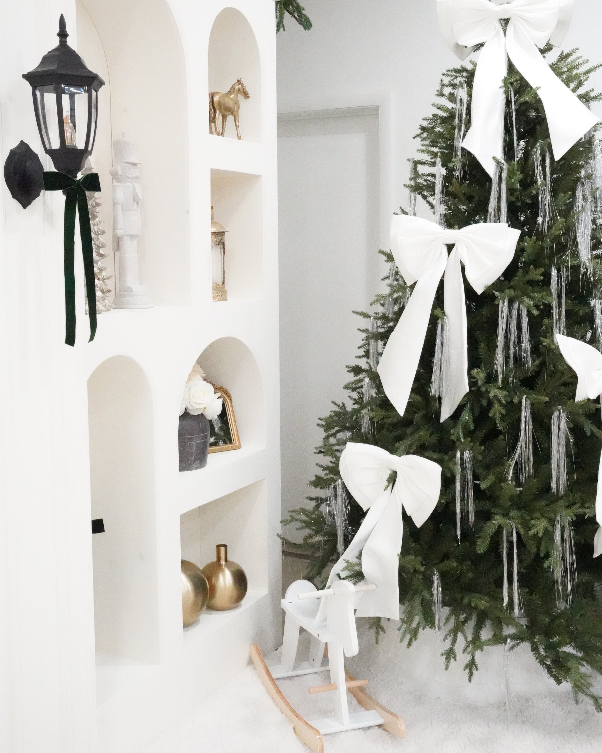 Christmas photo studio in Miami | Creative Canvas Photo Studio Miami Set de fotos navideñas en Miami caballito mecedor blanco bajo un árbol con lazos blancos gigantes