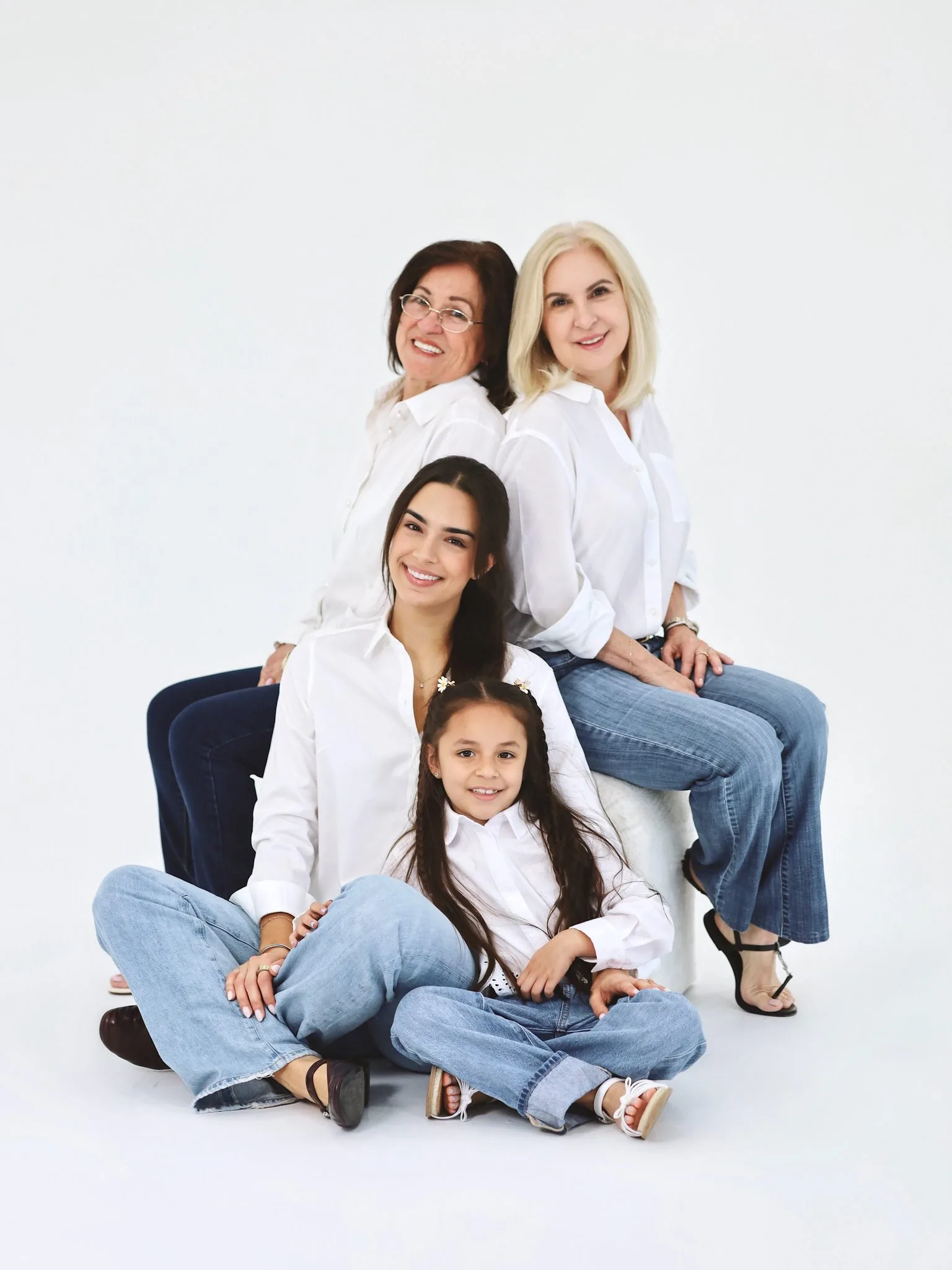 Family Photo Session Miami Photography Studio | White Denim | Creative Canvas Photo Studio Miami Sesión de fotos familiar en un estudio de Miami una niña y tres mujeres de su familia con camisas blancas y jeans sentadas