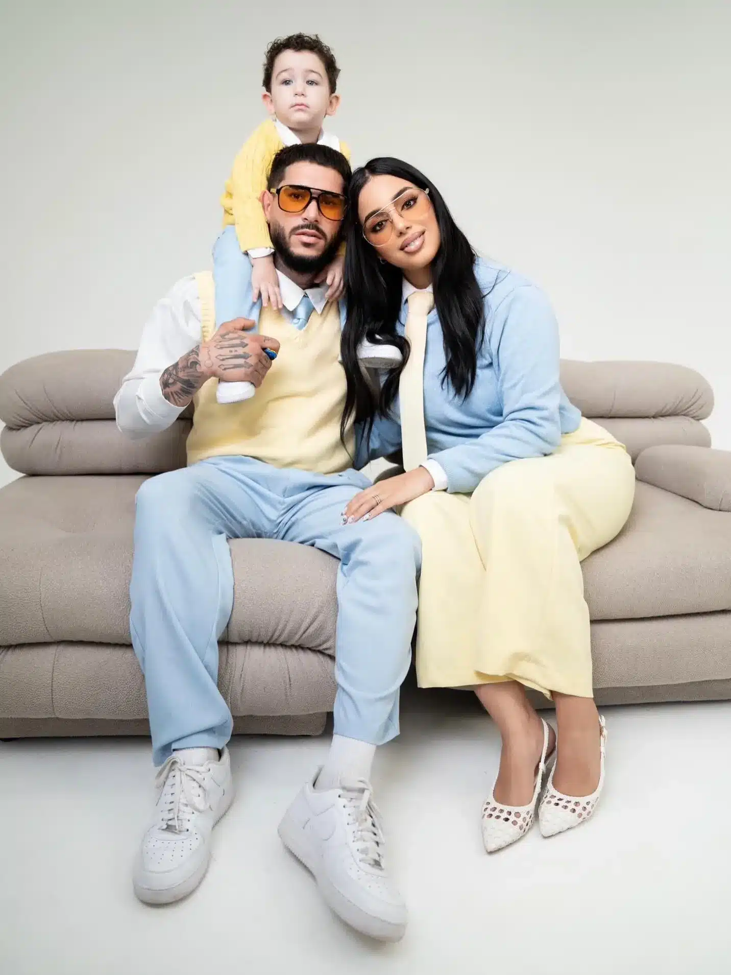 Family Photography Studio in Miami | Pastel Sofa Portrait | Creative Canvas Photo Studio Miami Fotos familiares en Miami padres de amarillo y azul pastel en un sofá gris con su hijo en los hombros del papá