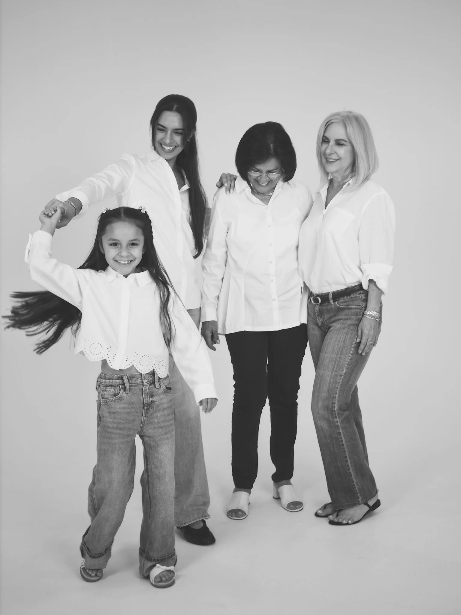 Family Pictures by a Miami Photographer | Black and White | Creative Canvas Photo Studio Miami Fotos de familia con fotógrafo en Miami niña sonriente girando junto a tres mujeres de su familia en blanco y negro
