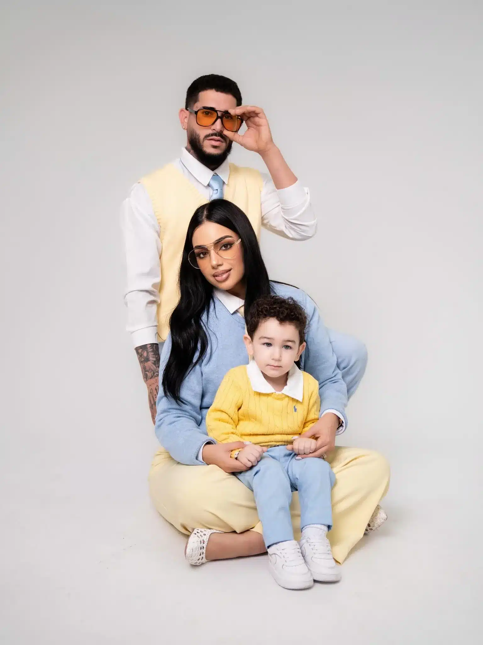 Family Portraits by a Miami Photographer | Pastel Outfits | Creative Canvas Photo Studio Miami Fotos familiares con fotógrafo en Miami padres con ropa pastel combinada y su hijo de suéter amarillo en el regazo de mamá
