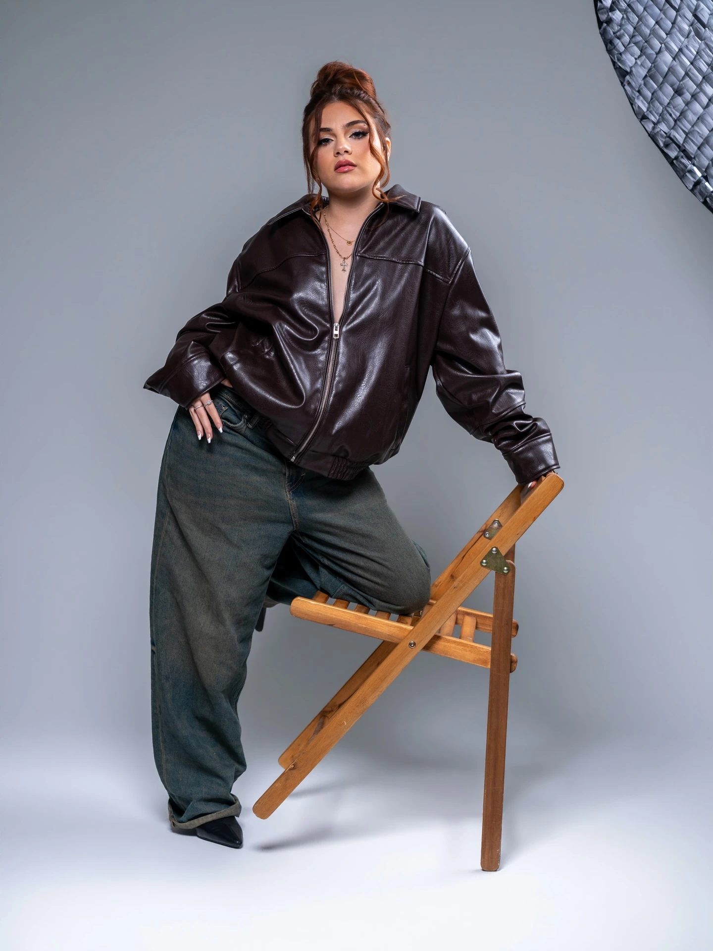 Fashion photography studio in Miami | Creative Canvas Photo Studio Miami Book fotográfico en Miami chaqueta de cuero marrón y jeans anchos de rodillas sobre una silla