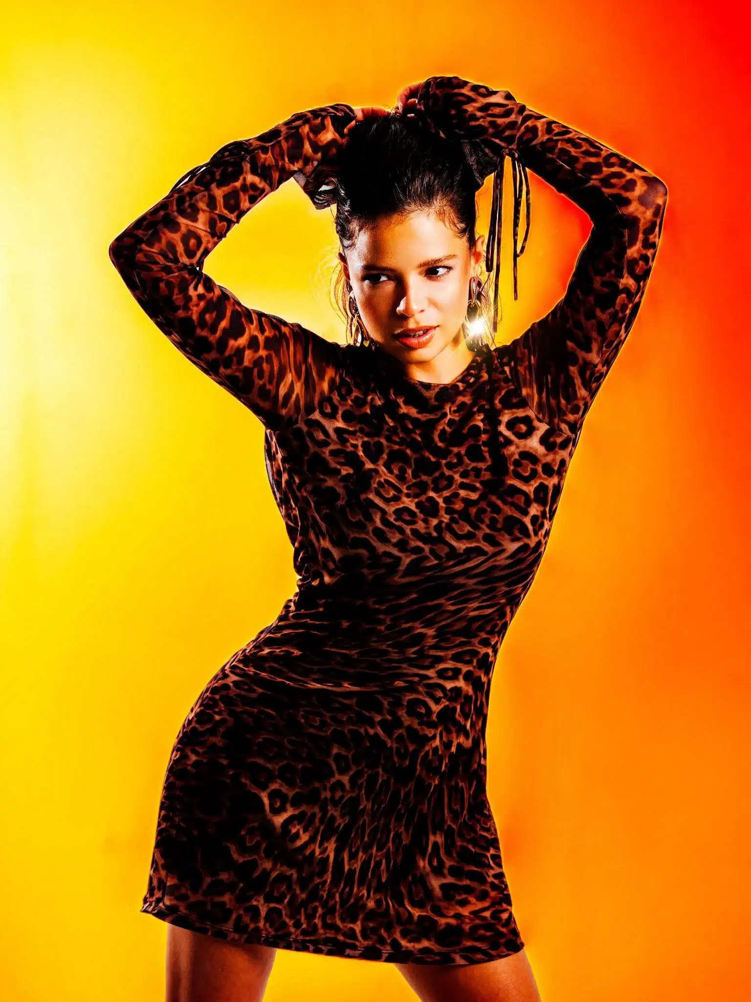 Sesión de fotos de moda en Miami mujer con vestido de leopardo y brazos en alto bajo luz naranja